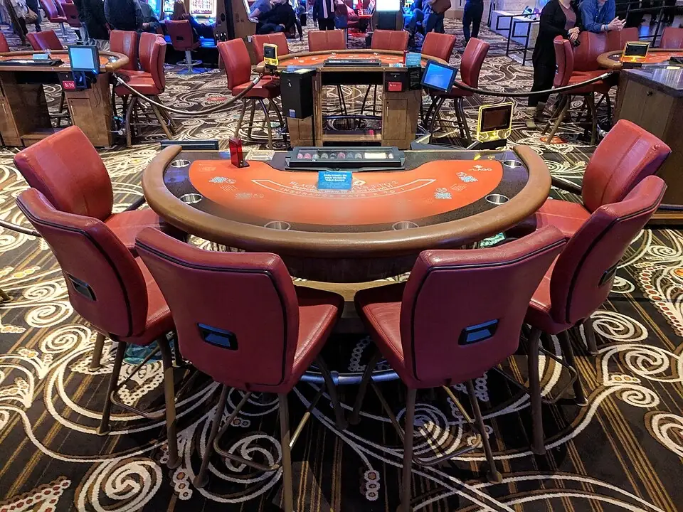 Félkörös blackjack-asztal piros kárpitozott székekkel egy kaszinóteremben