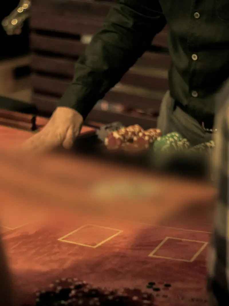 Osztó keze egy blackjack-asztal fölött, félhomályos kaszinóban