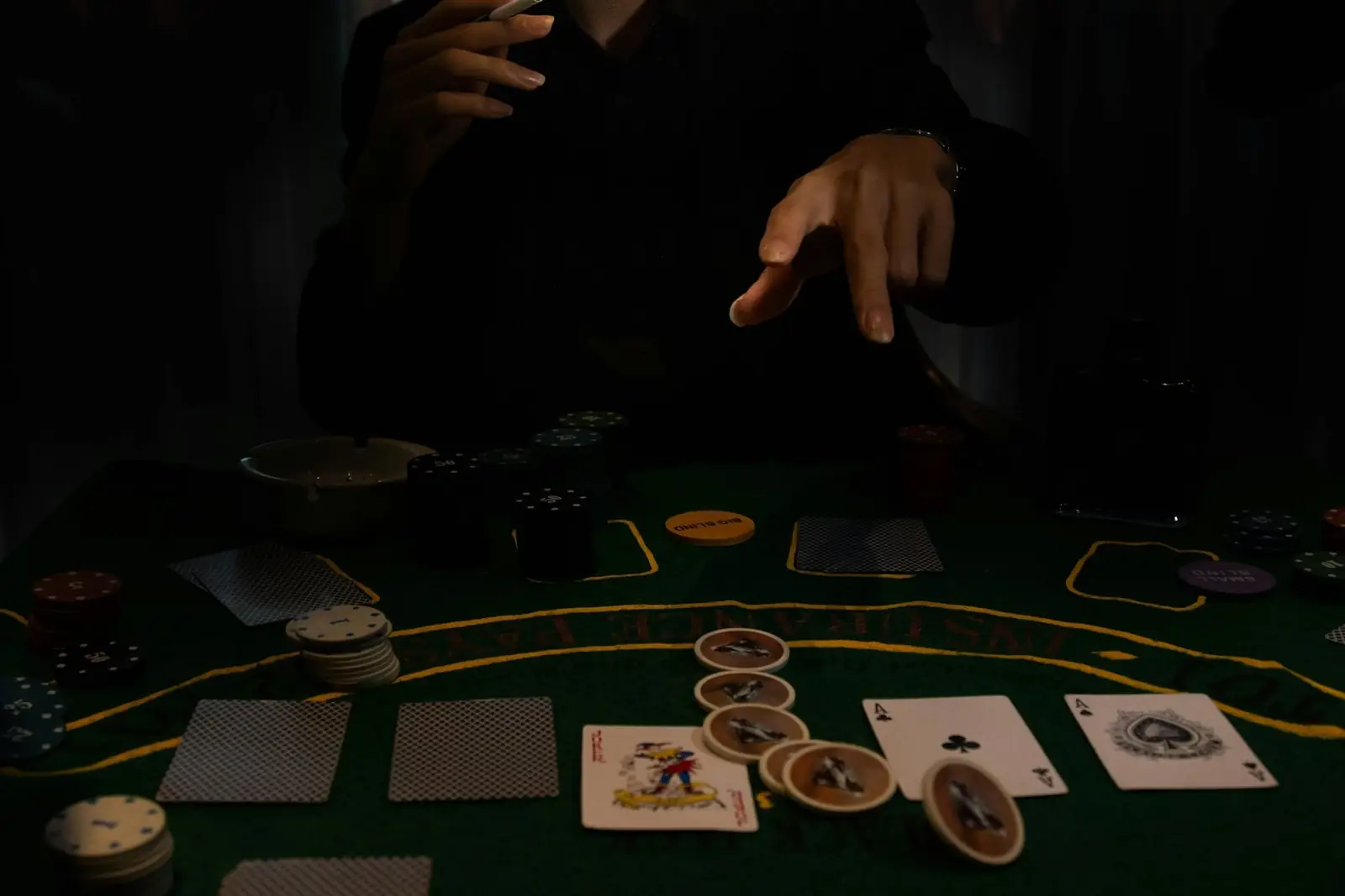 Sötét blackjack-asztal zöld filccel, kártyalapokkal és zsetonokkal, fölötte egy játékos keze