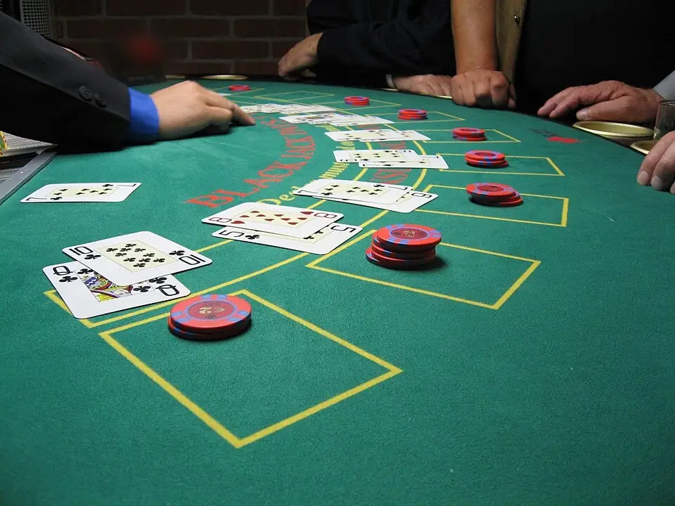 Zöld filces blackjack-asztal közelről, kártyalapokkal, zsetonokkal és sárga helyjelölő mezőkkel